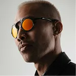 Man with short blond hair wearing reflective orange sunglasses and a black shirt.