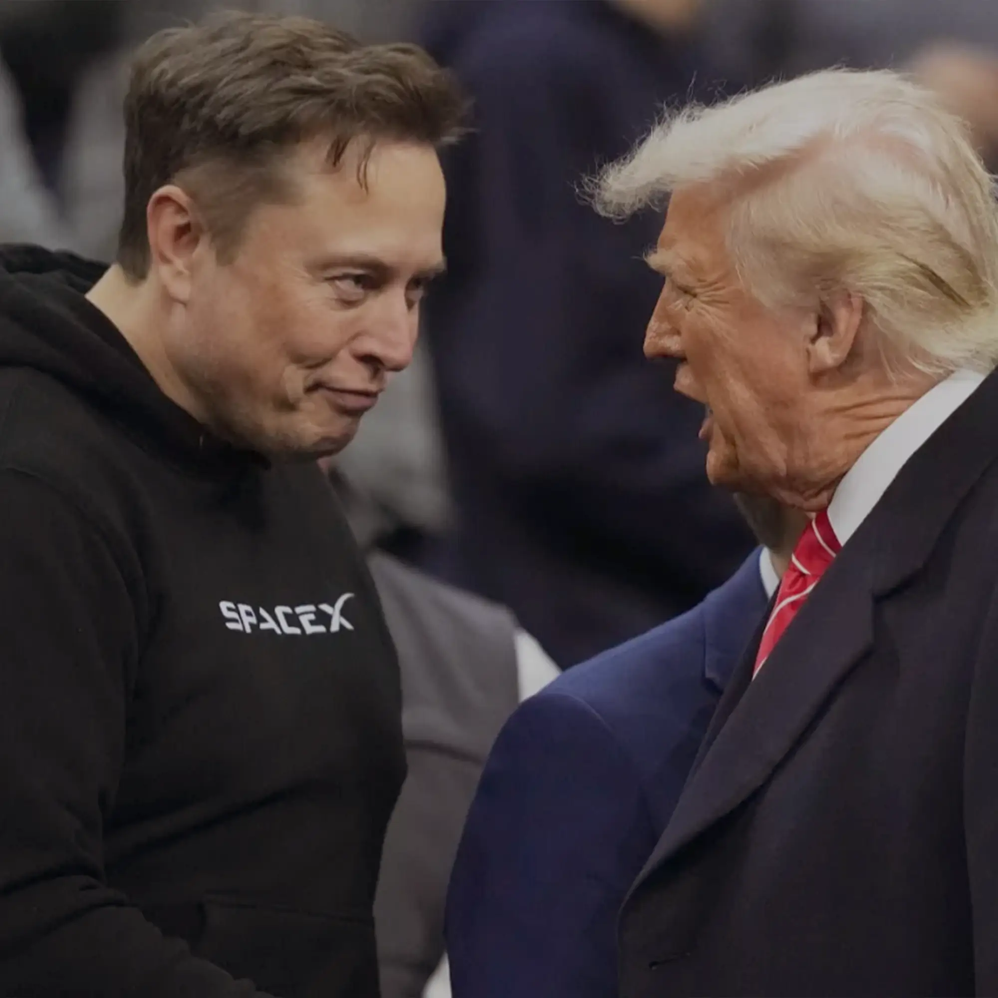 "Elon Musk and Donald Trump talking during a public event, highlighting their political and economic rivalry."