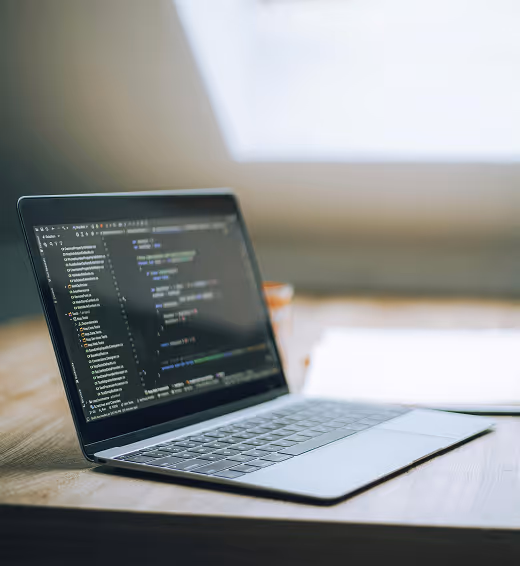 Laptop on wooden table displaying code editor with programming code near bright window.