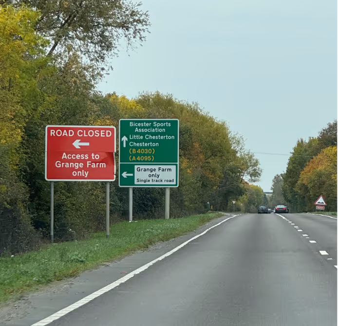 Two road signs by a country road indicating road closure to Grange Farm and directions to Bicester and Chesterton.