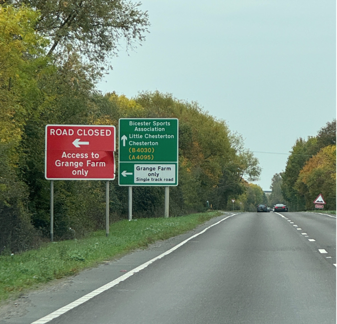 Two road signs by a country road indicating road closure to Grange Farm and directions to Bicester and Chesterton.