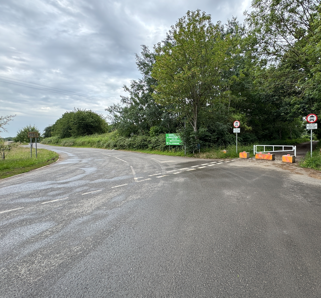 Fork in a rural road with green trees, a white barrier, and traffic signs restricting vehicle access.