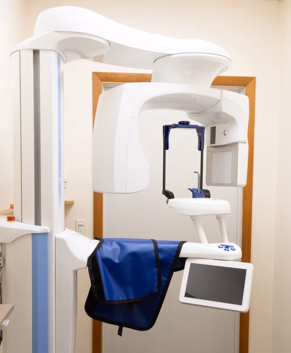 Dental 3D imaging machine with blue protective apron and attached monitor in a clinical room.