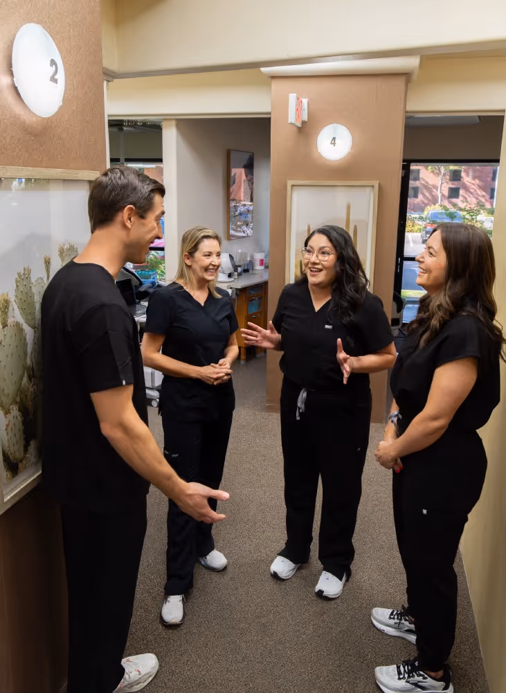 Four healthcare professionals in black scrubs smiling and talking in a clinic hallway.