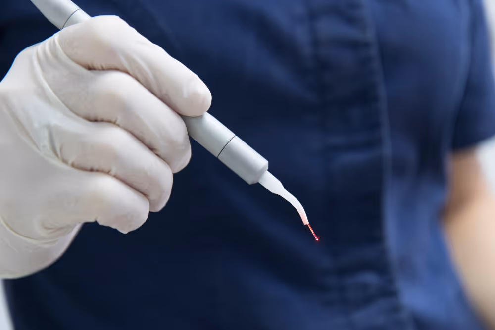 Hand in latex glove holding a dental laser tool emitting a small red laser light.