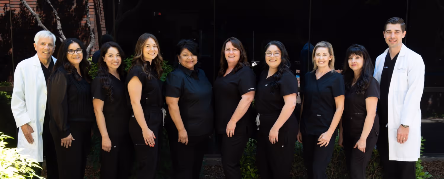 Group of medical professionals in black and white uniforms standing outdoors, smiling at the camera.