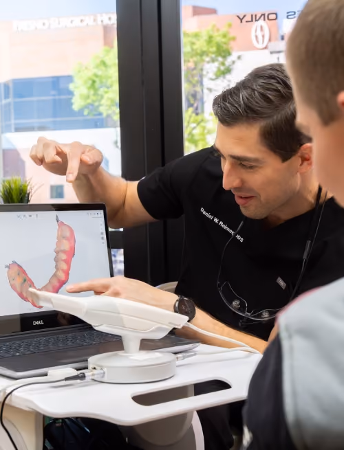 Dentist showing patient a 3D dental model on a laptop screen in a bright office.