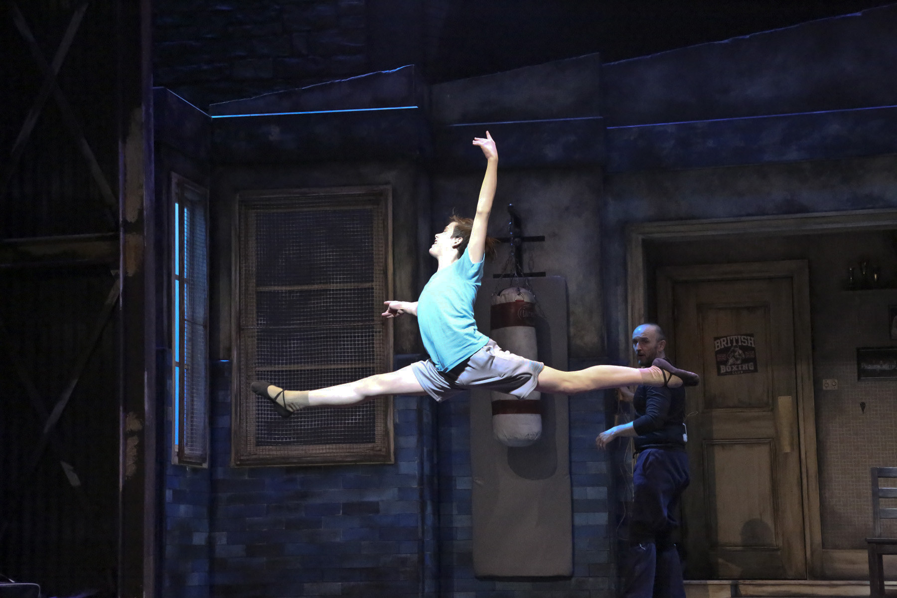 Production photo from Billy Elliot showing Billy leaping across the stage in a dance sequence.