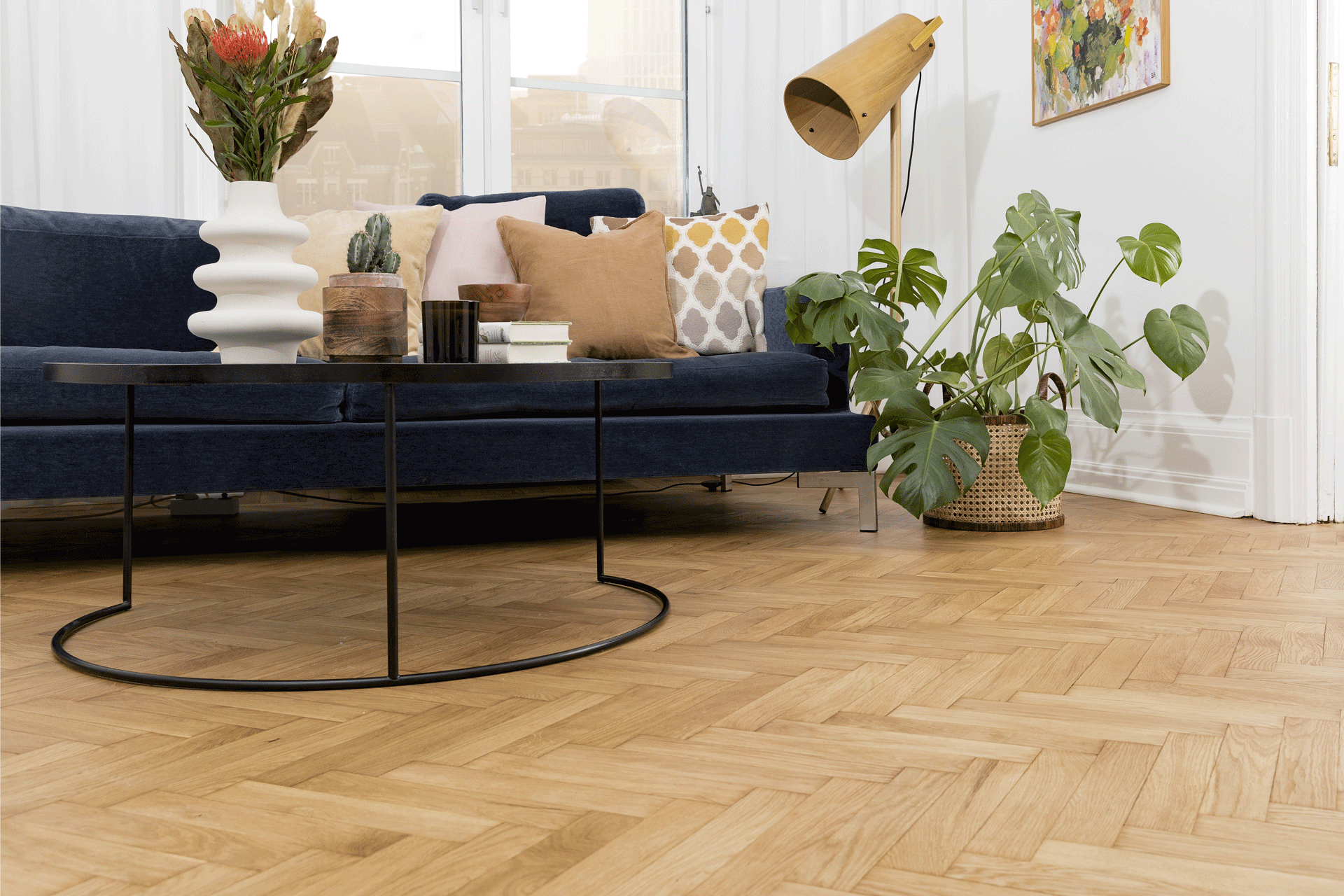 Modern living room with navy sofa, patterned cushions, black round coffee table, and large green plant in basket.