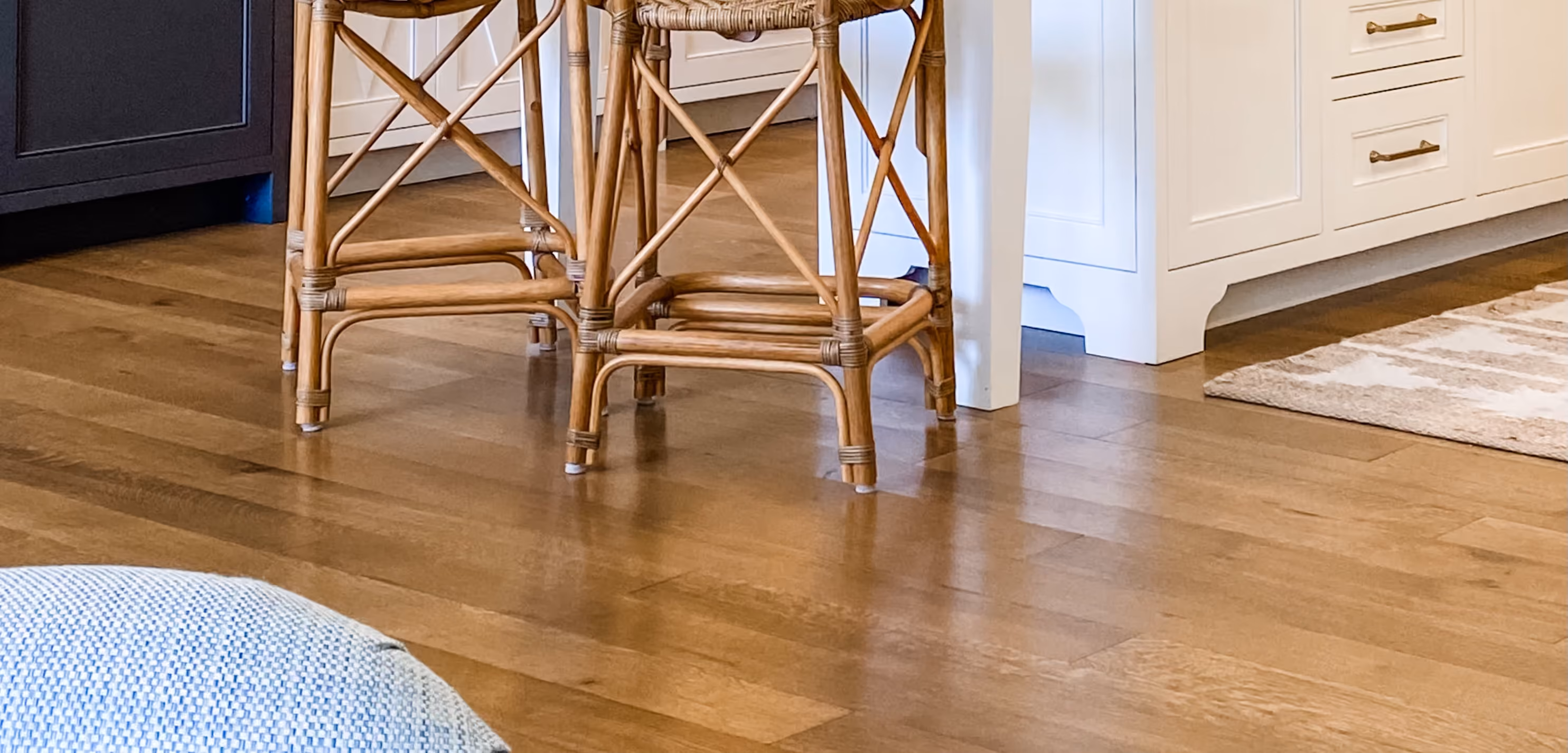 Wooden stool legs on polished hardwood floor under white kitchen cabinets and island.