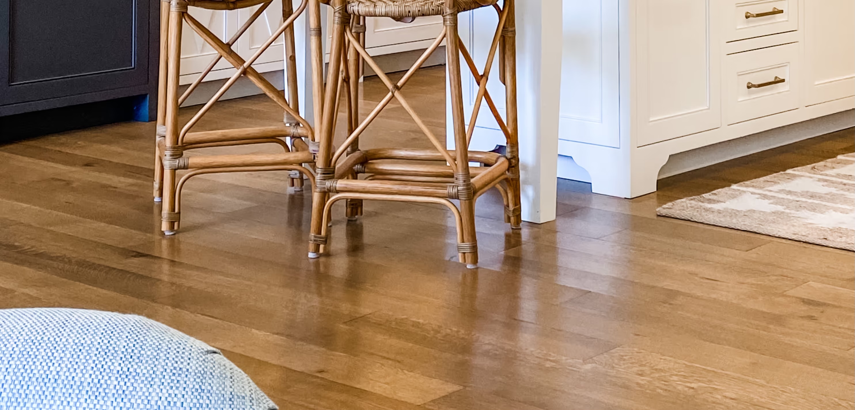 Wooden stool legs on polished hardwood floor under white kitchen cabinets and island.