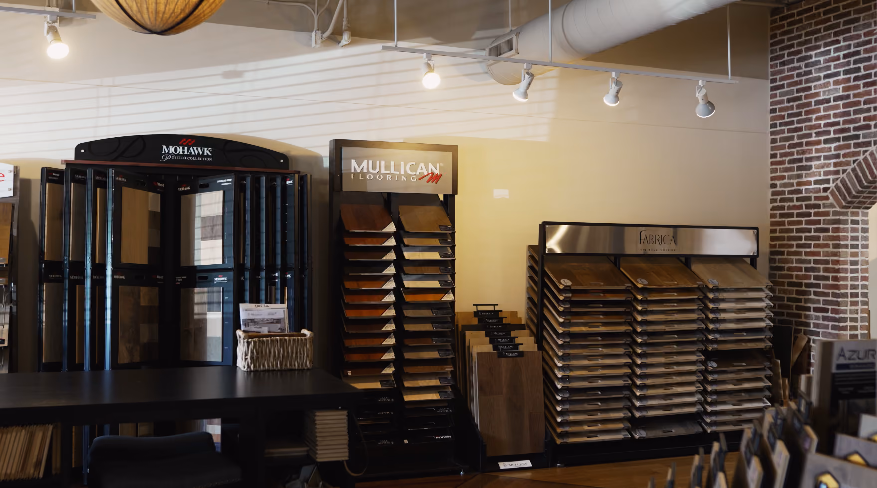 Showroom with wood flooring samples from Mohawk, Mullican, and Fabrica brands on display racks.