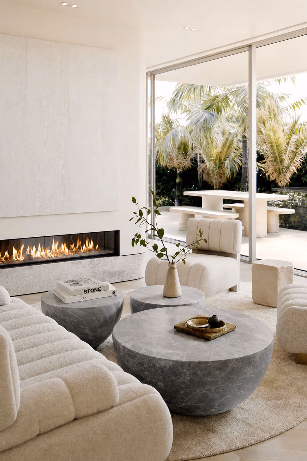 Living area fireplace detail with sculptural marble coffee tables and view to travertine outdoor dining setting