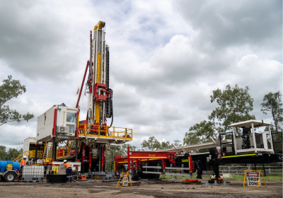DRS 200 is set up outdoors under a cloudy sky, with the mast fully raised and support equipment positioned around the base. The rig sits among sparse trees, with safety railings and operational platforms visible, highlighting a