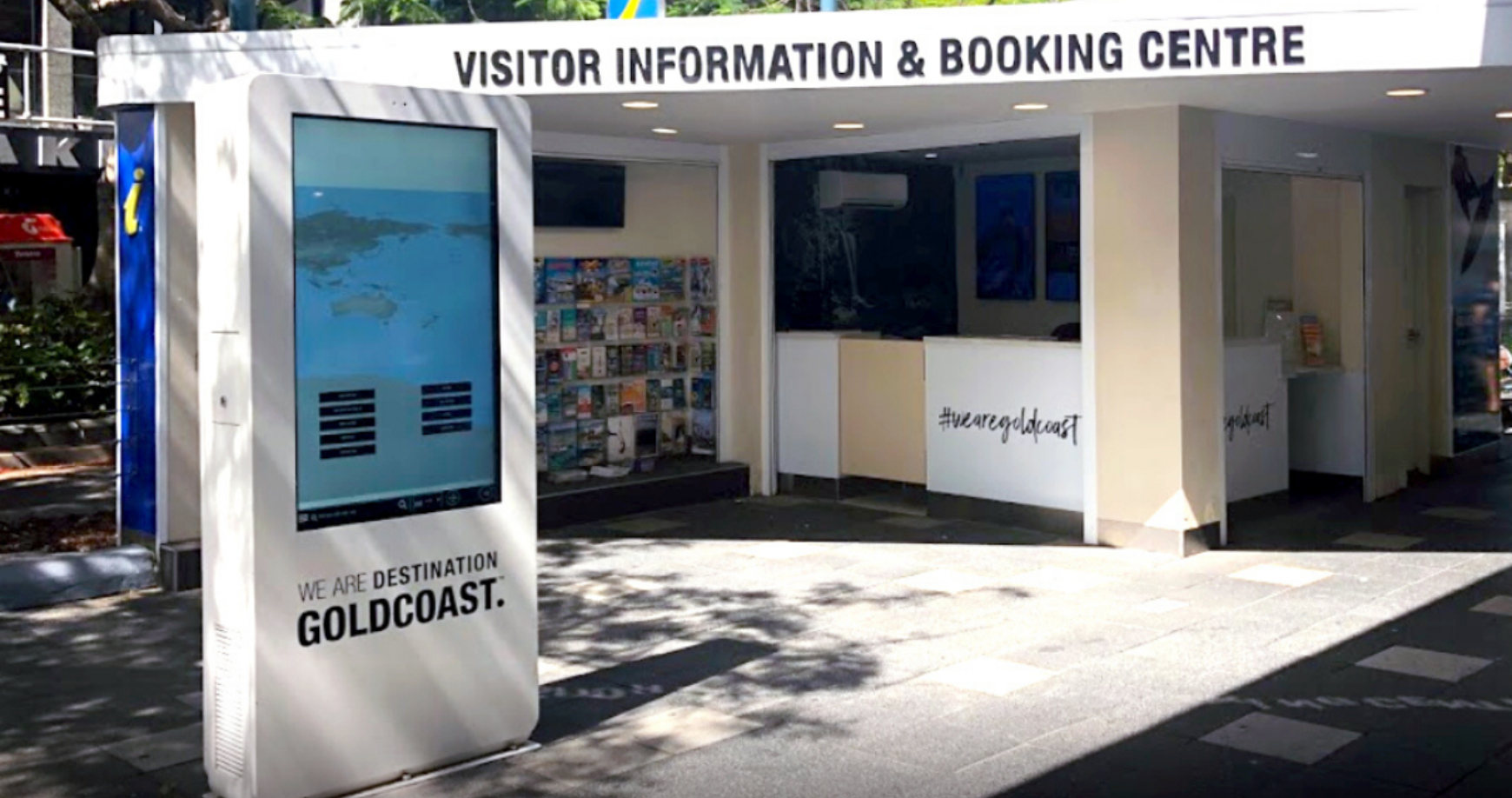Outdoor visitor information and booking centre with a digital kiosk displaying a map and brochures inside, branding indicates Destination Gold Coast.