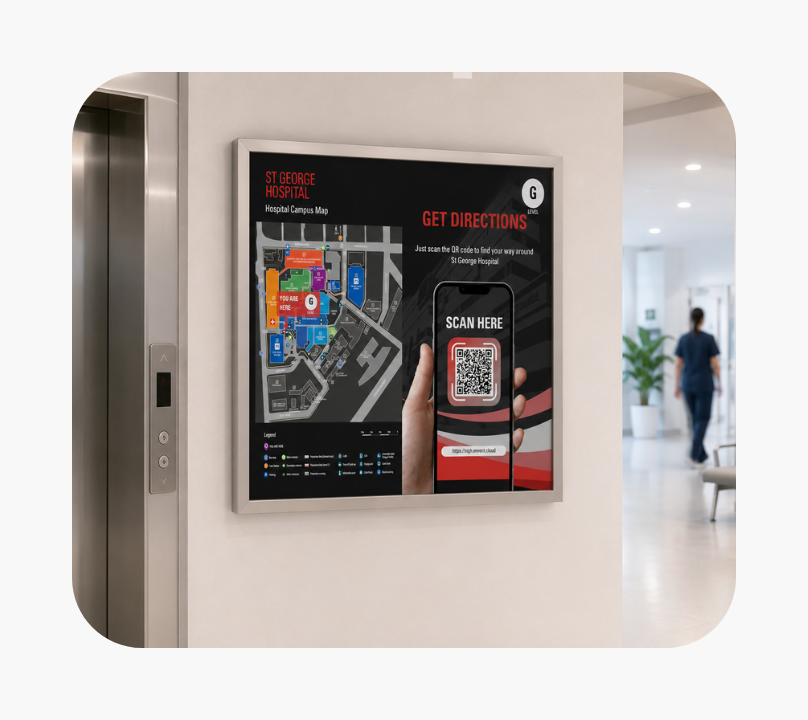 Indoor hospital hallway with a wall-mounted digital sign next to an elevator. The sign displays a St George Hospital campus map on the left and a phone screen showing a QR code on the right, with text instructing viewers to scan the code for directions. A person in medical scrubs walks down the hallway in the background.