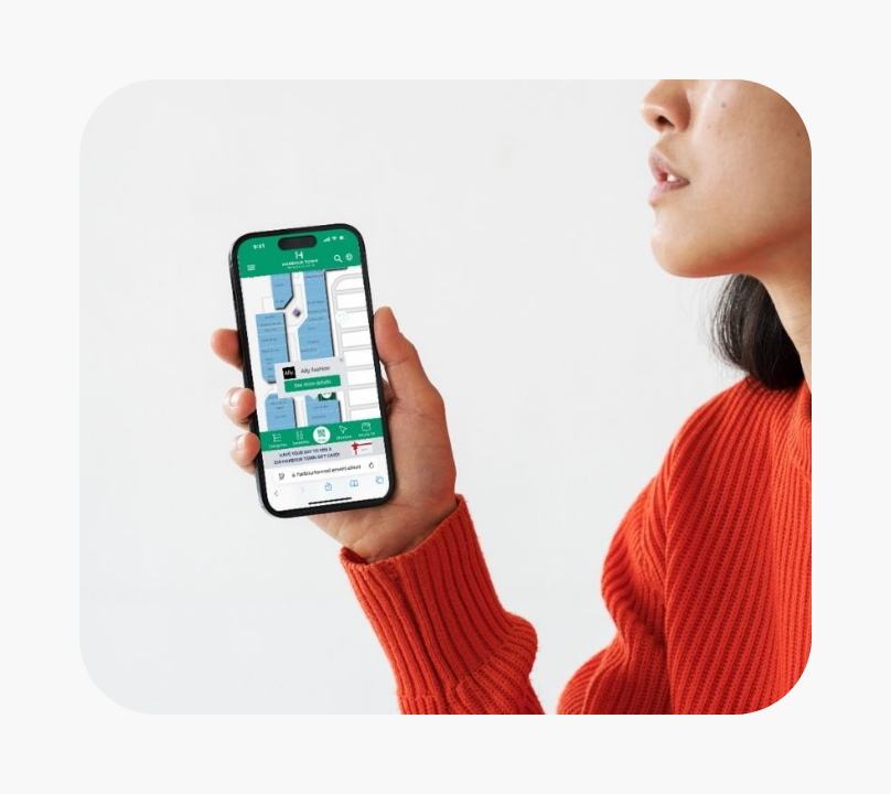 Person wearing an orange sweater holding a smartphone displaying a digital map for wayfinding in a shopping area.