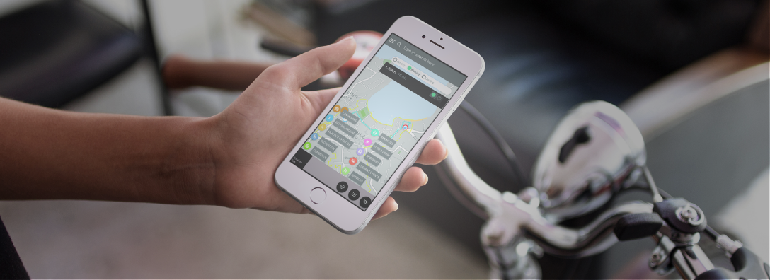 Person holding a smartphone displaying a navigation app showing a map with routes and points of interest, next to bicycle handlebars.