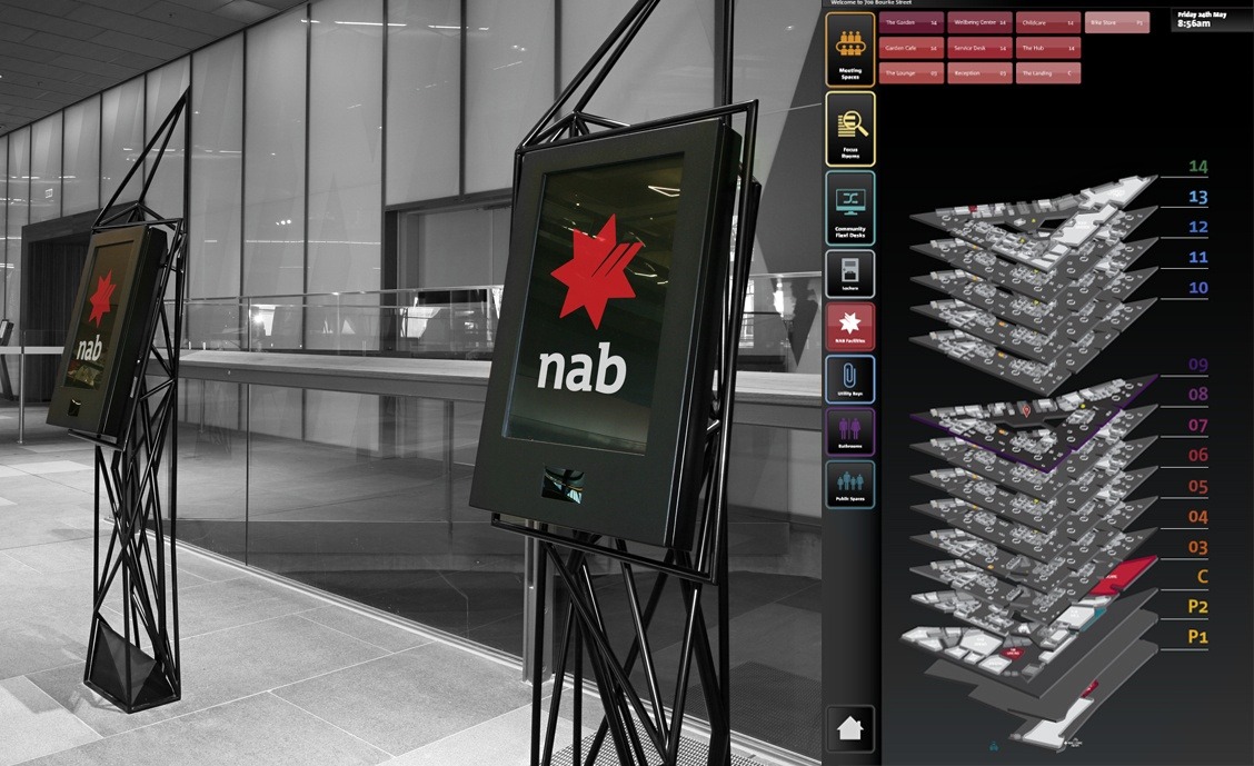 Black and white photo of an indoor modern building lobby with two digital display stands featuring the red star and 'nab' logo, next to a digital directory map showing multiple floor levels and facility options.