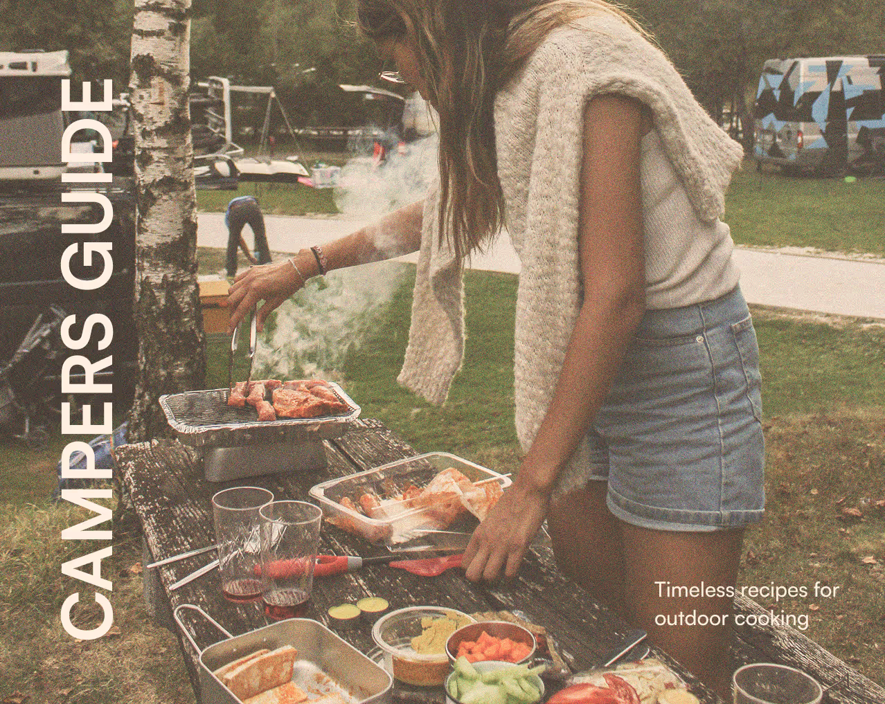 Woman grilling meat on a portable grill outdoors with various food items on a weathered wooden table.
