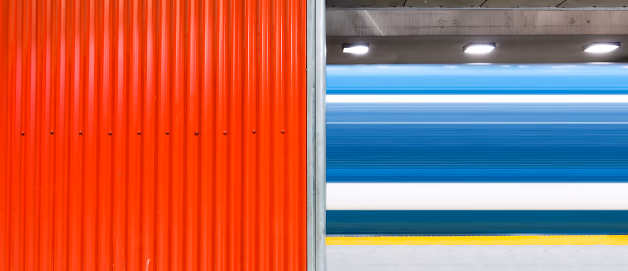 Metro beside a vertical red corrugated metal wall under ceiling lights.
