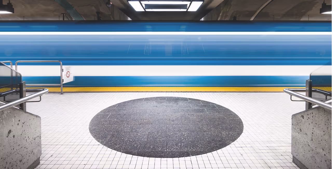 Blurred blue and white train passing through a subway platform with circular dark tile pattern.
