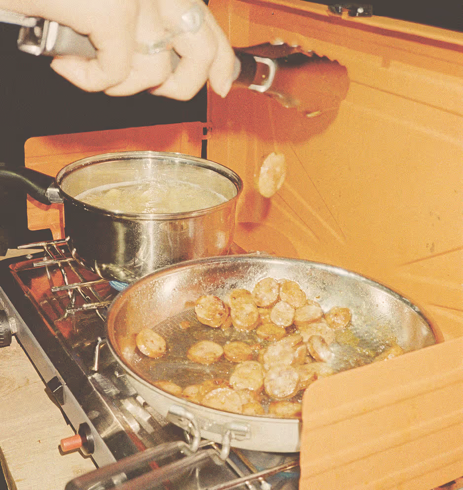 Hand using tongs to cook sliced sausage in a frying pan on a gas stove.