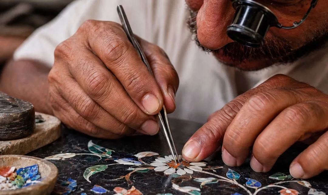 Artisan using tweezers and a magnifying loupe to set coloured stone pieces into a Pietra Dura floral inlay on black marble