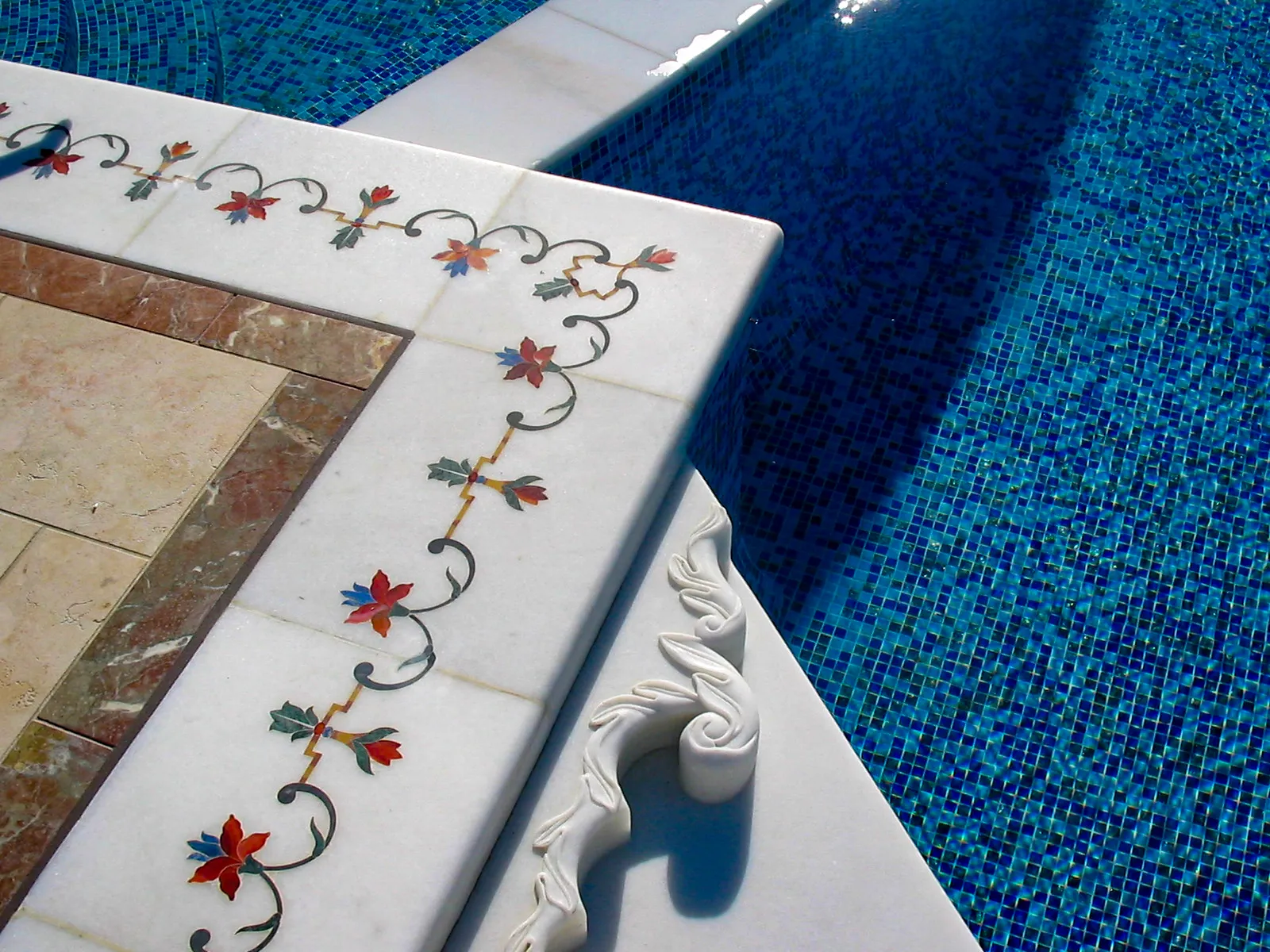 Pietra dura floral inlay of semi-precious stones on a white marble pool coping beside blue mosaic tiles, The Los Altos Hills Estate