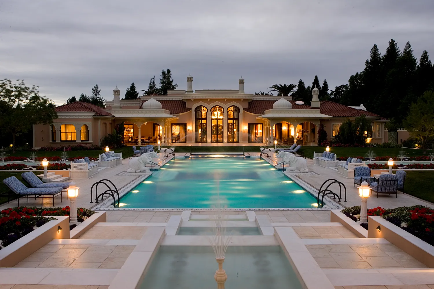 Estate at dusk with a long pool, marble water-channel fountains and lit lanterns leading to the house, The Los Altos Hills Estate, California