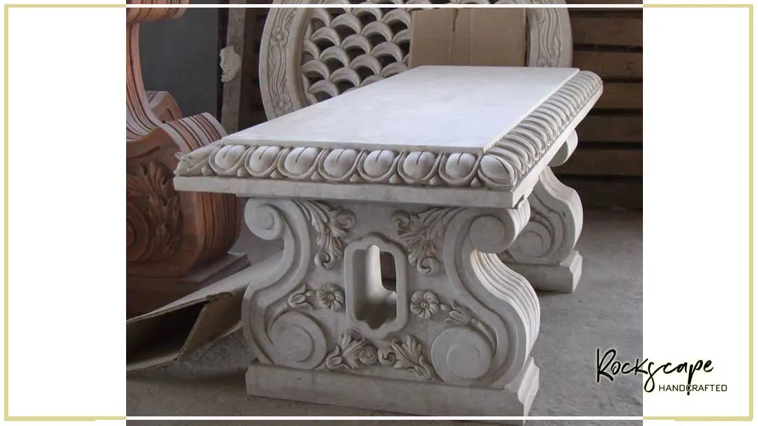 Hand-carved white marble garden bench with scrolled legs and a jali screen behind it