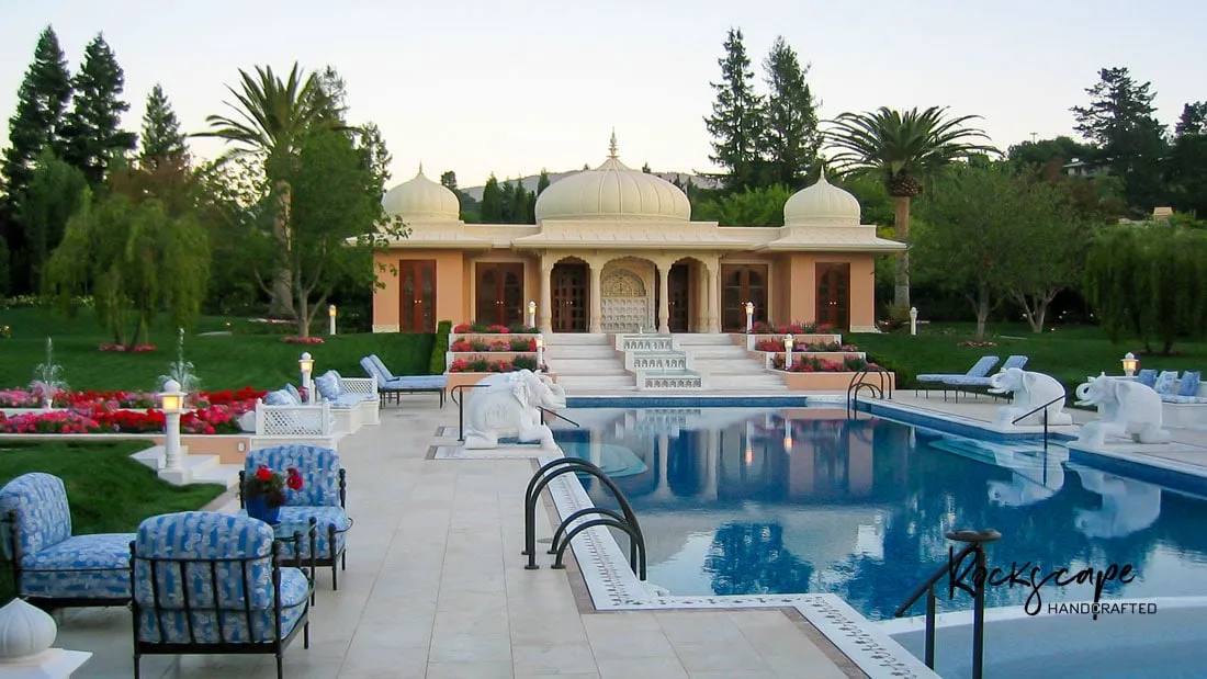 Resort-style estate pool with blue loungers in front of domed Mughal-style pavilions