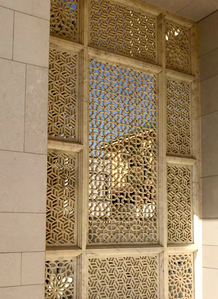 Floor-to-ceiling hand-carved marble jali screen panels set into a stone wall at the Al Mula Residence, Kuwait