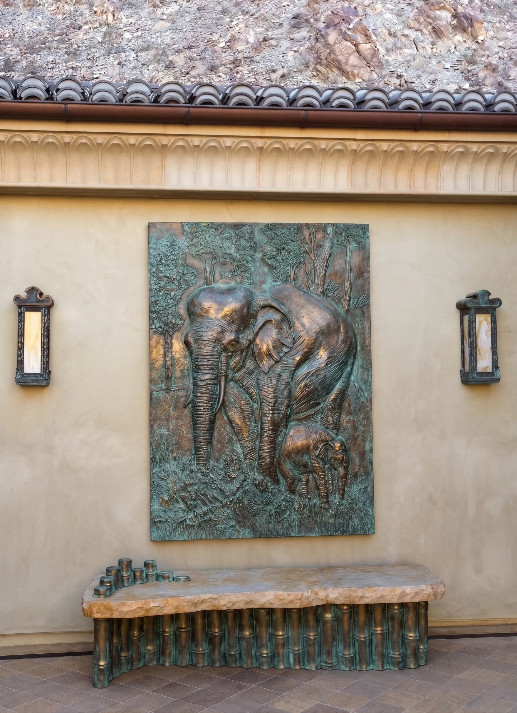 Bronze elephant relief panel mounted above a stone bench between wall lanterns, Desert Sanctuary, Palm Springs