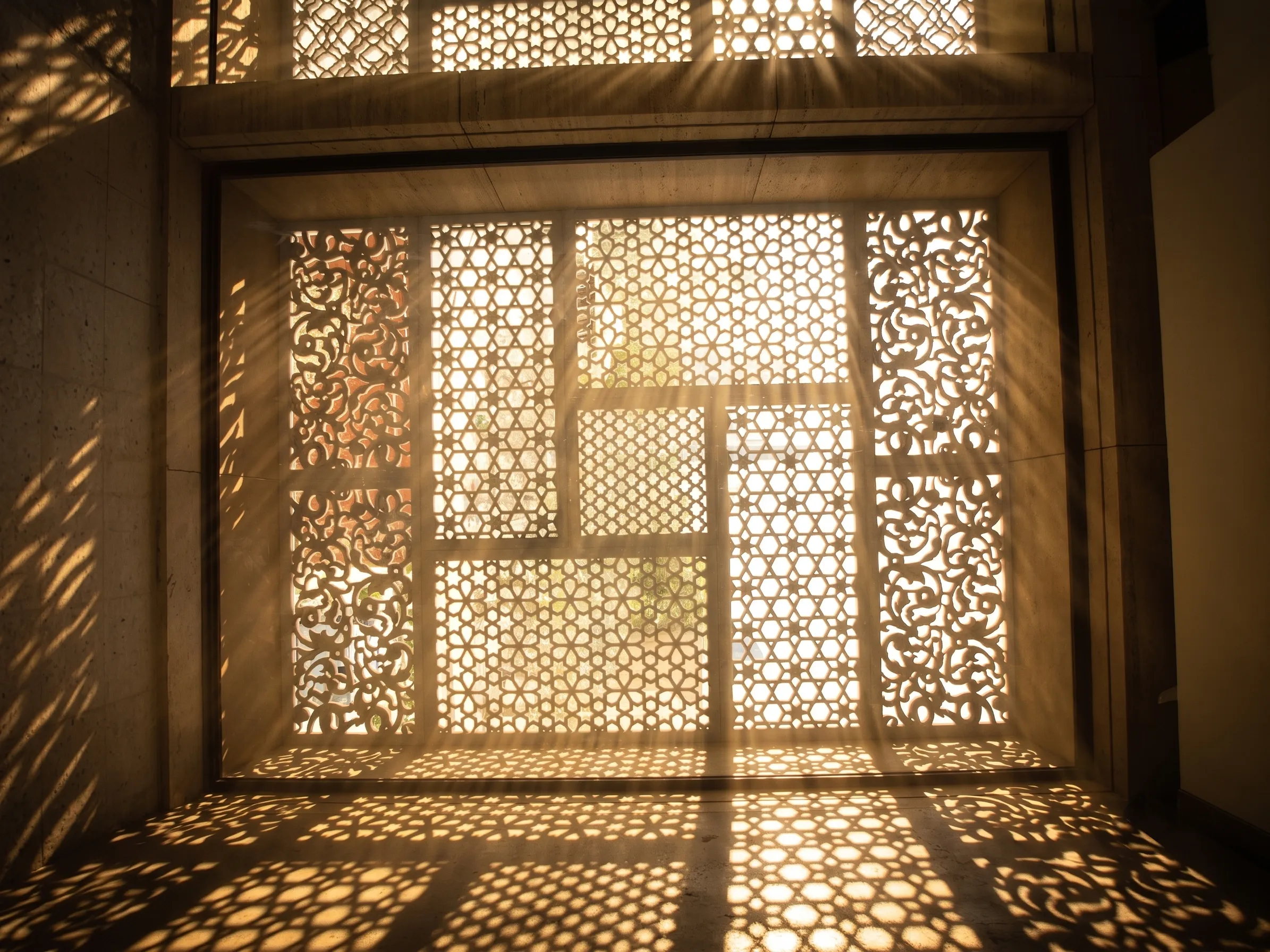 Sunlight streaming through a full-height carved stone jali screen into an interior room, Elite Residence, Kuwait
