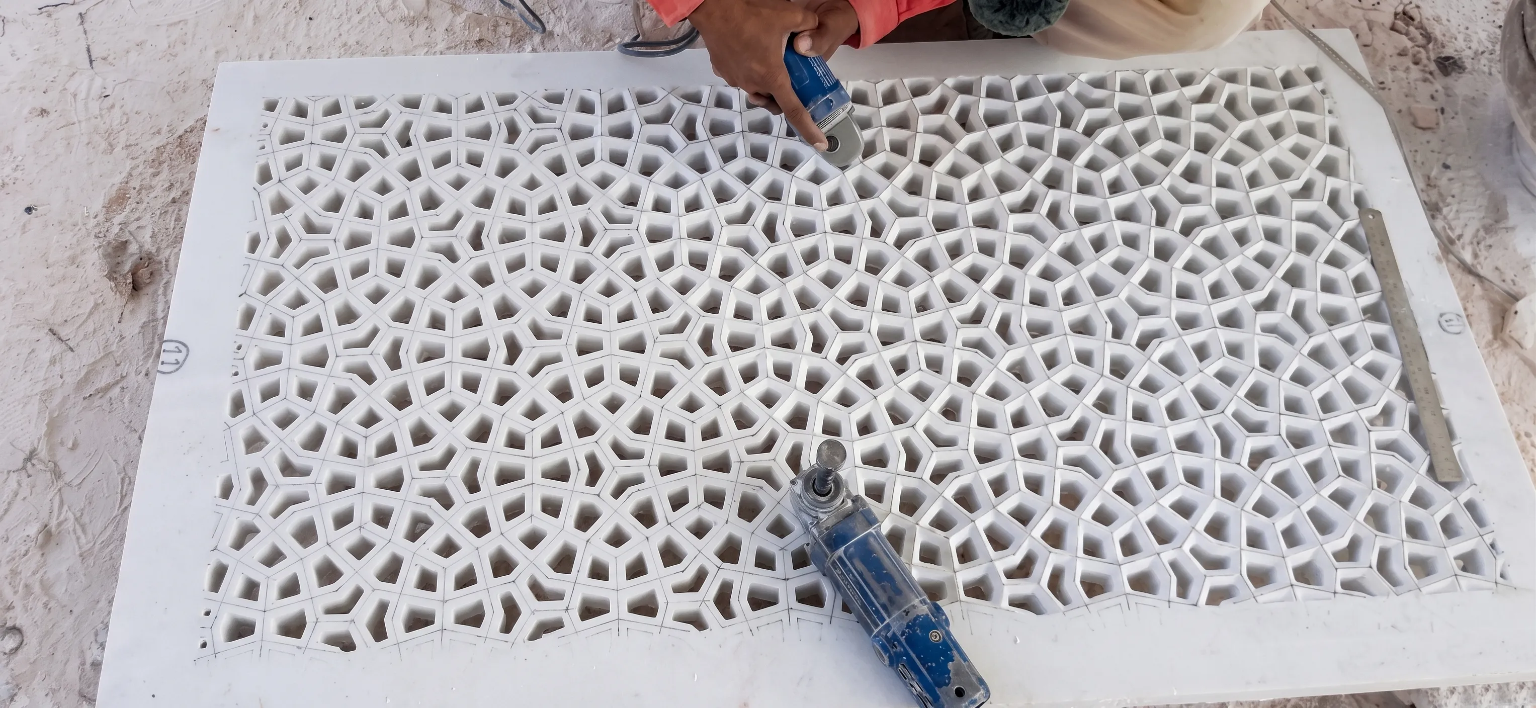 Artisan using a hand tool to cut a fine geometric marble jali panel for The Plaza Residence