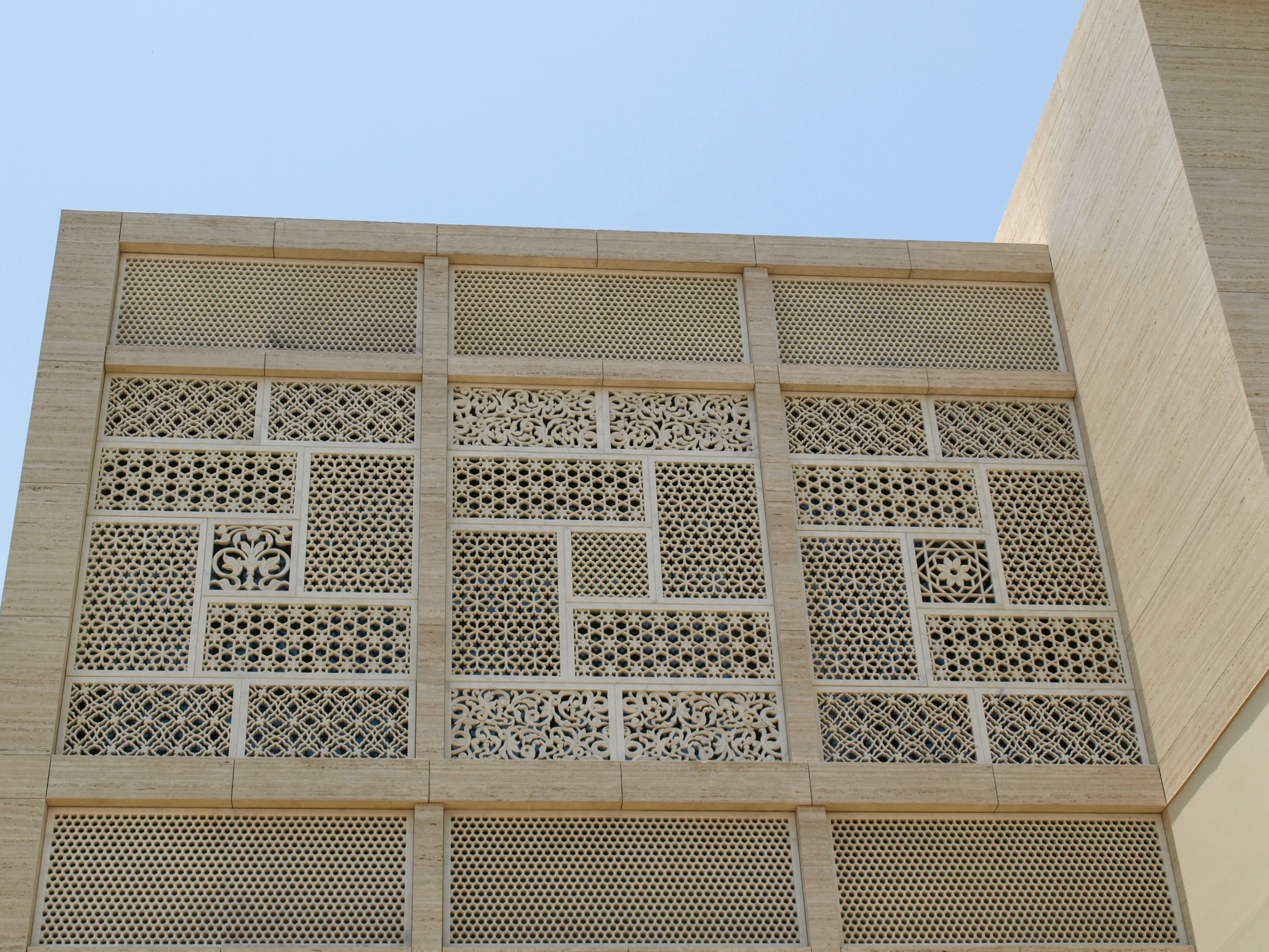Carved stone jali panels across the upper storey of the Elite Residence, Kuwait, against a blue sky
