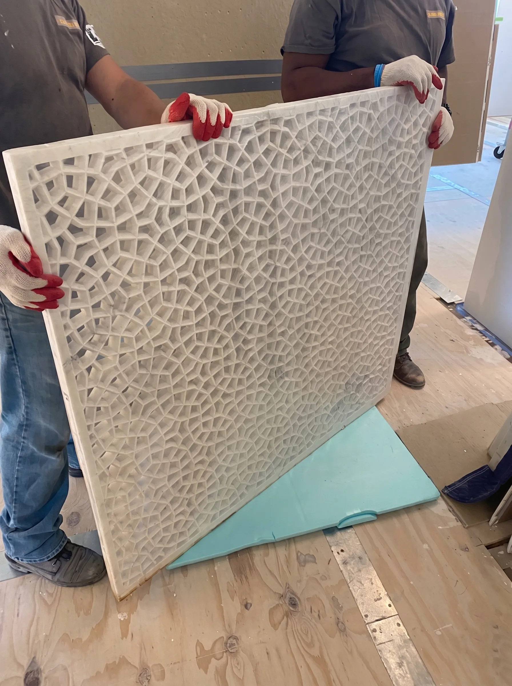 Two installers in gloves lifting a carved marble jali panel at The Plaza Residence
