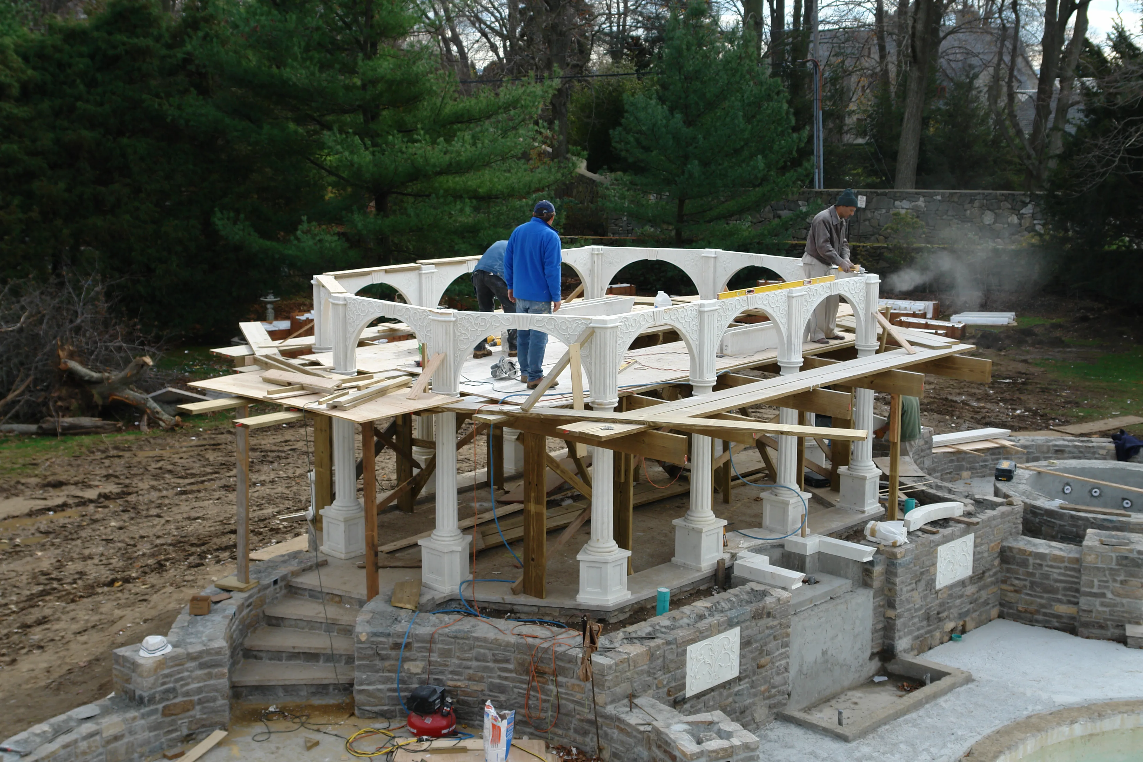 White marble pavilion under construction with timber roof framing and stone terrace walls, Westport, Connecticut estate