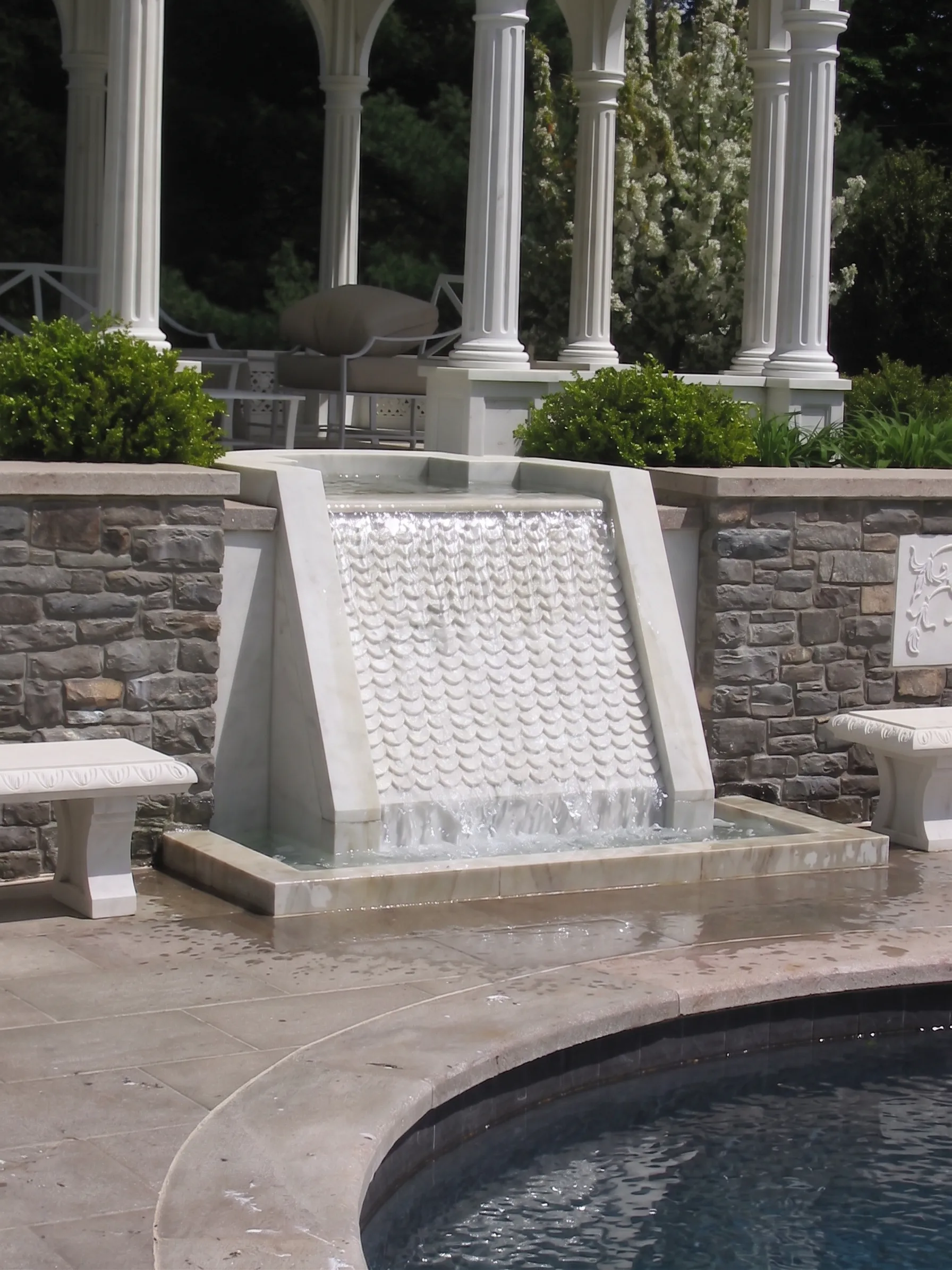Carved white marble waterfall spilling into the swimming pool beside stone seating walls, Westport, Connecticut estate