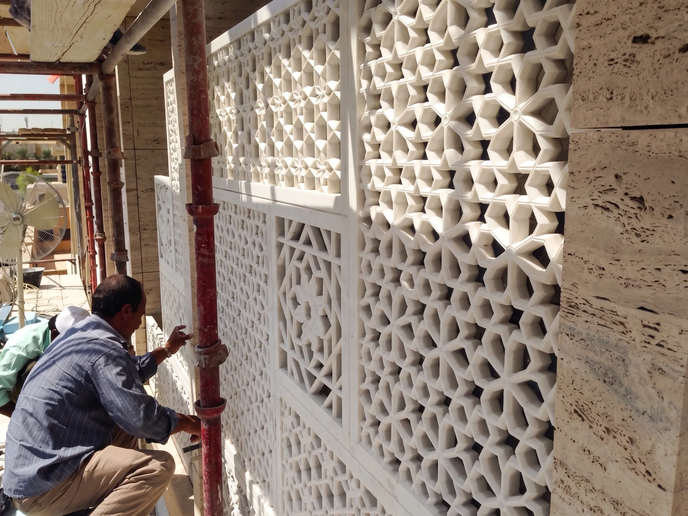 Installer fixing a curved-pattern stone jali panel to the facade of the Elite Residence, Kuwait