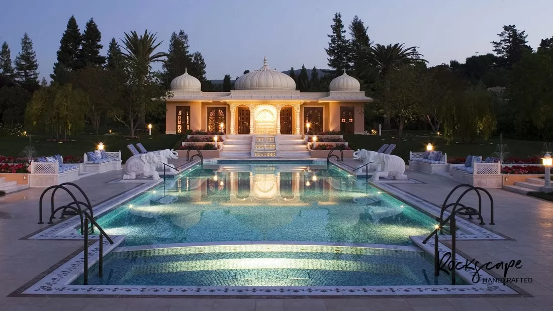 Floodlit pool at dusk leading to a white domed marble pavilion with chhatris