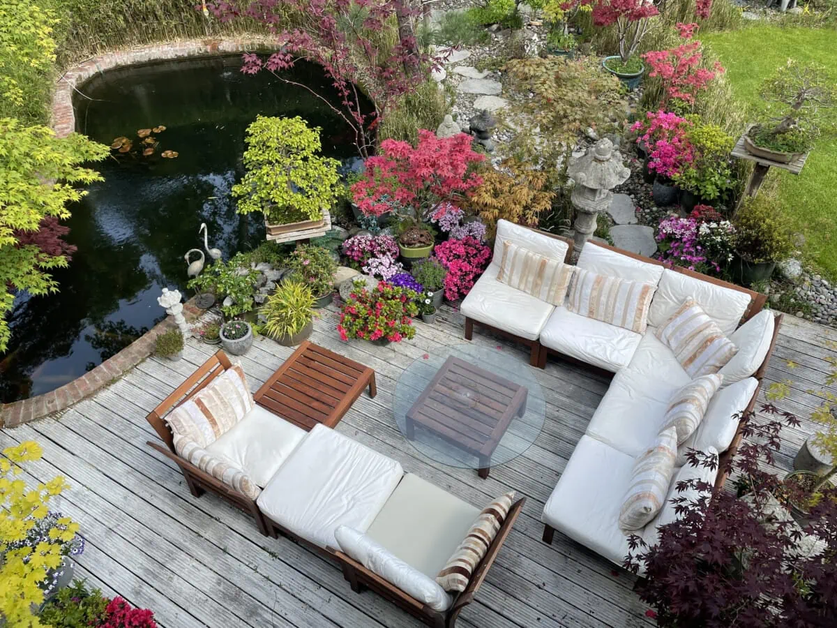 Outdoor sectional sofa on a timber deck beside a garden pond and flowering shrubs