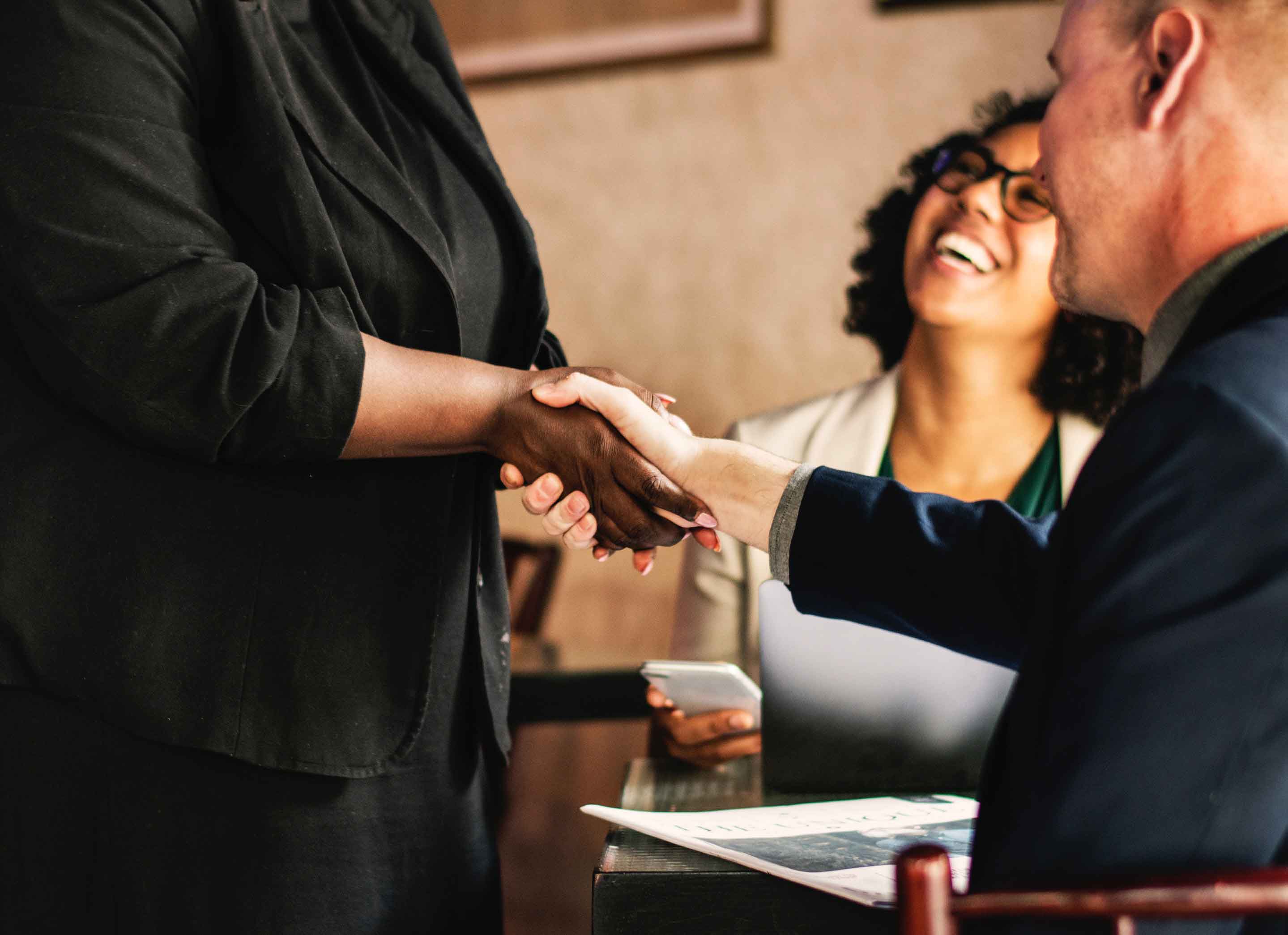 Woman shaking a mans hand with lady in background smiling