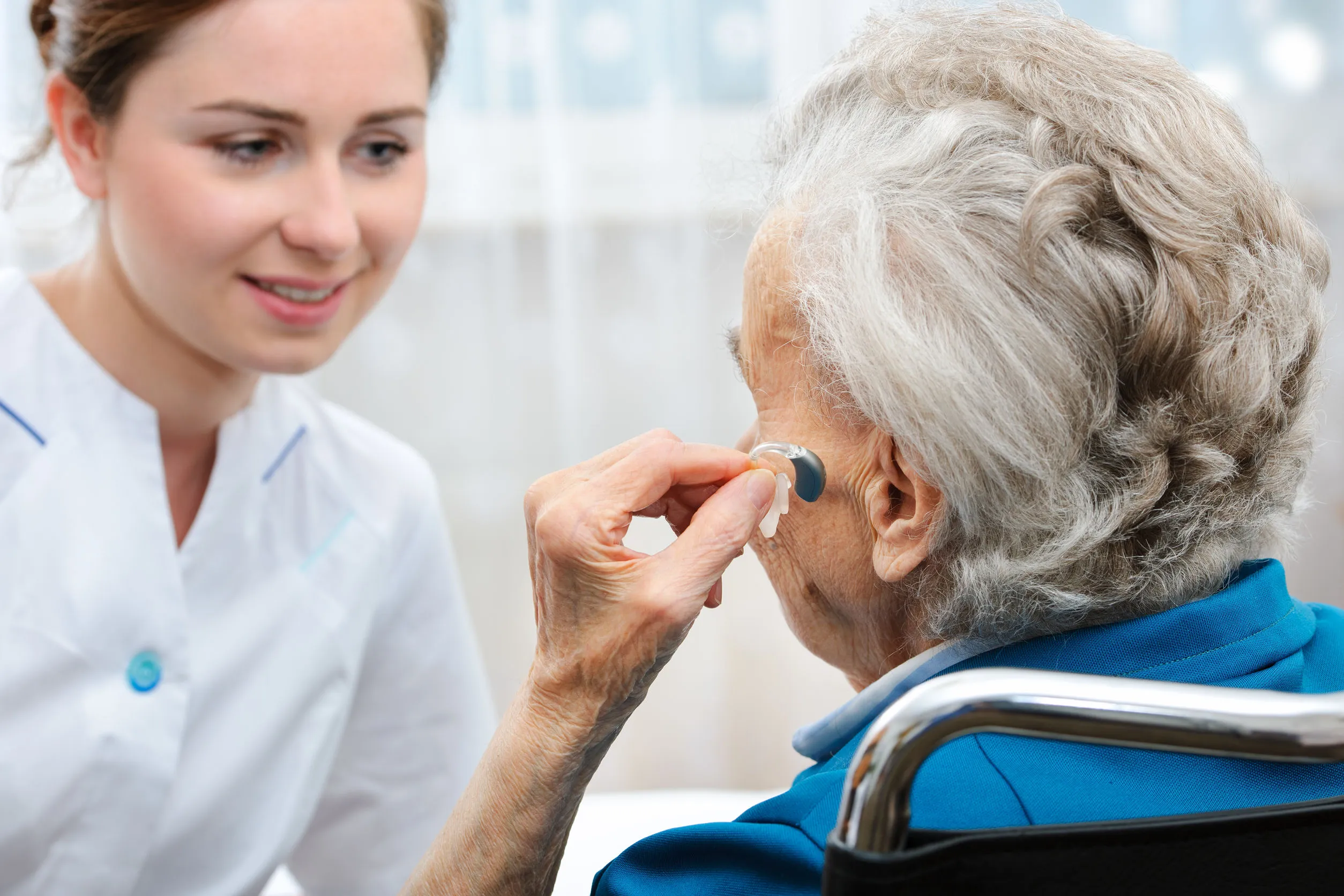 Senior woman inserts hearing aid in her ear