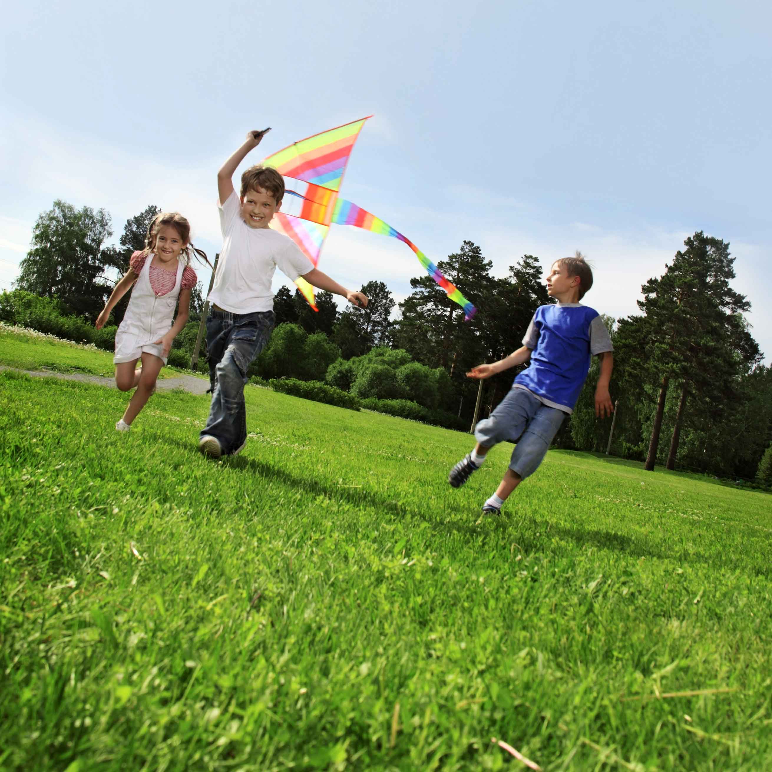 Three children running in the grass with a colorful kite