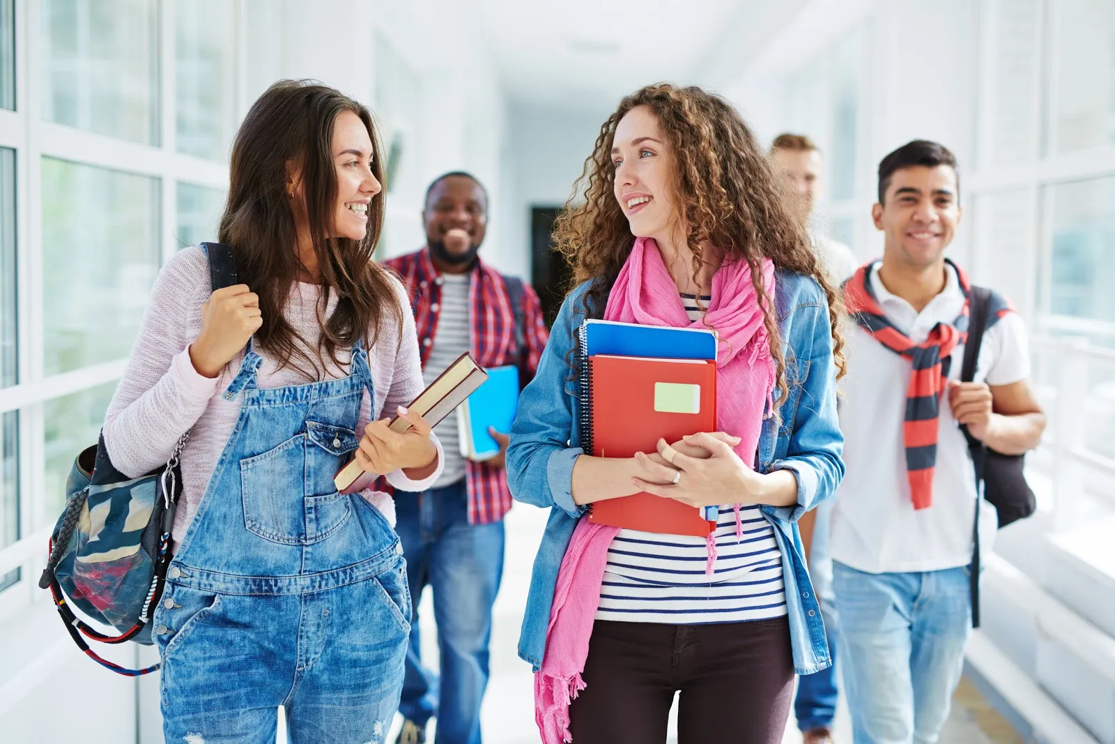 Two cute students walking along college corridor and talking after classes