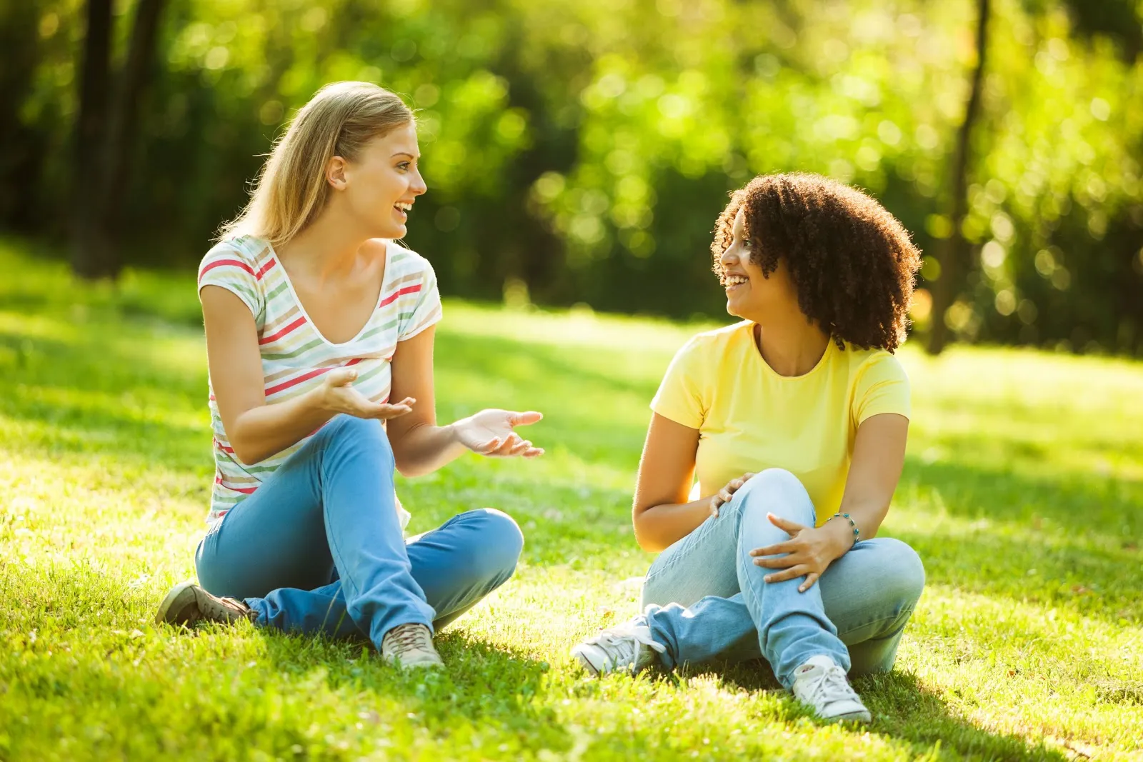 two girls sitting in the grass outside talking speech easy