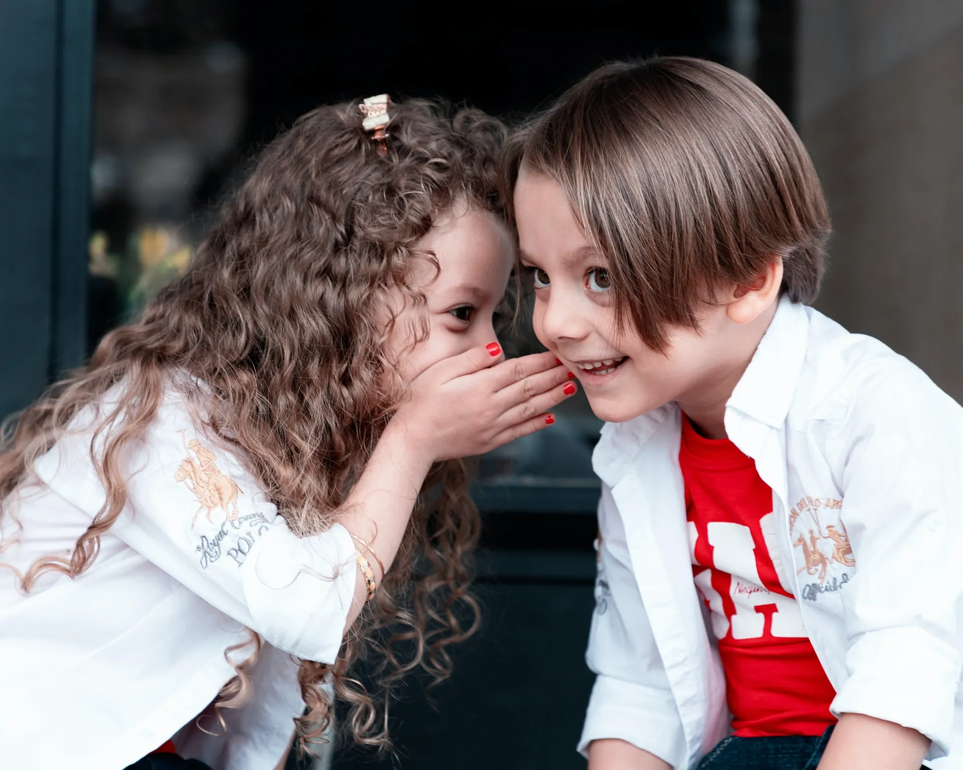 Two children whispering to one another using speech stuttering therapy.