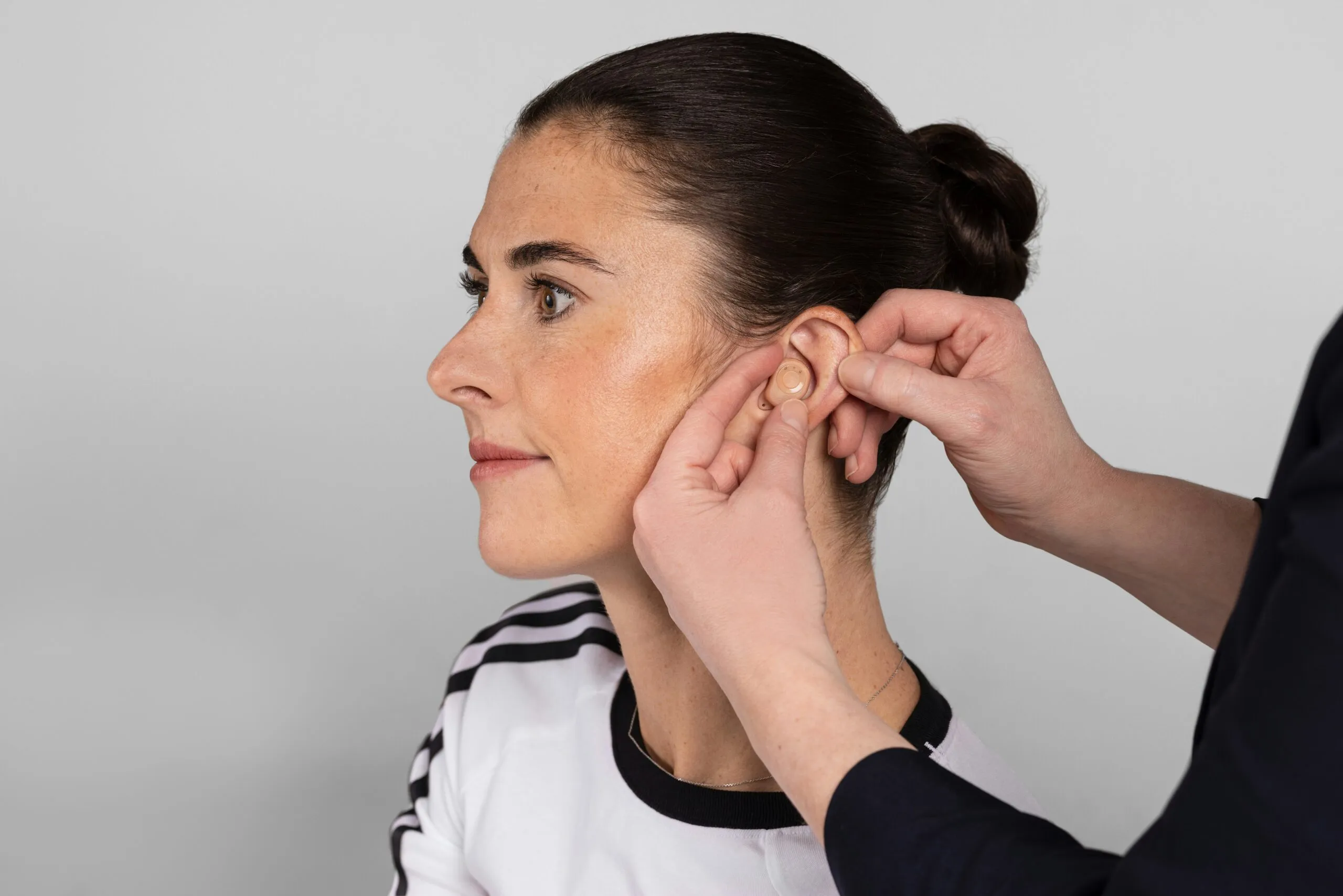 A person fitting a hearing aid into a woman's ear.